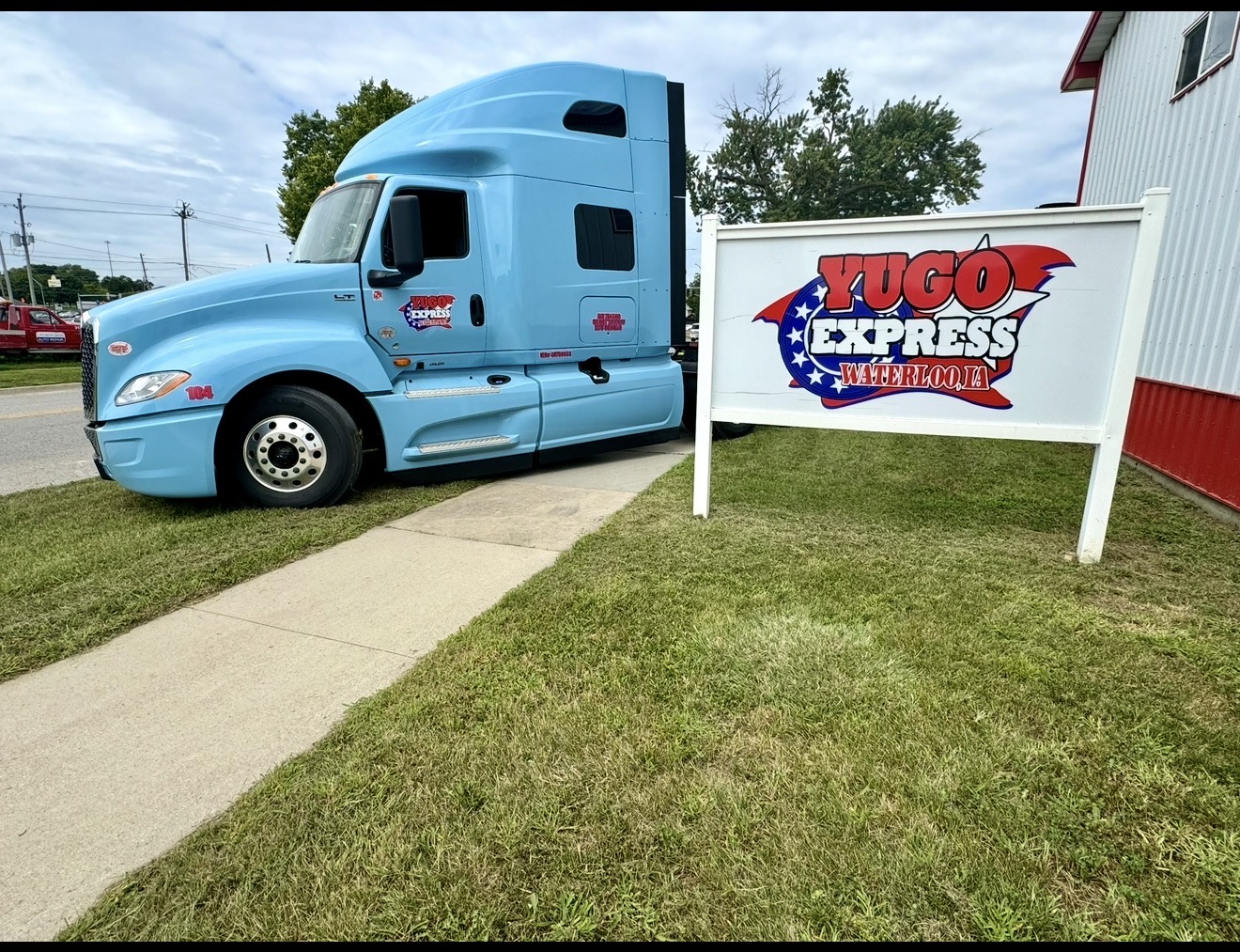 Blue Yugo Express semi truck beside the original company sign